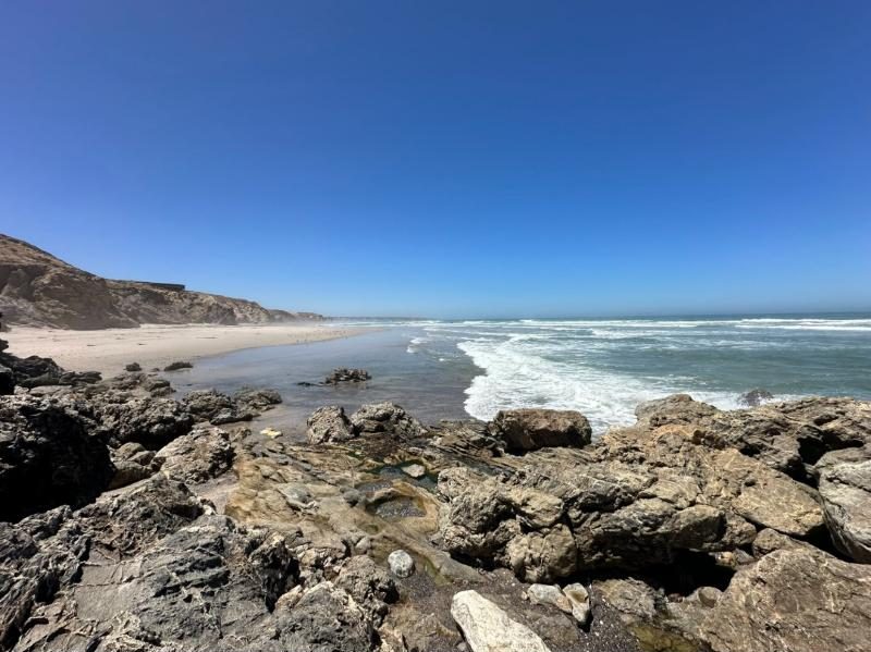 Rocky shoreline on the Atlantic coast with white surf rolling onto a long sandy beach under a clear blue sky